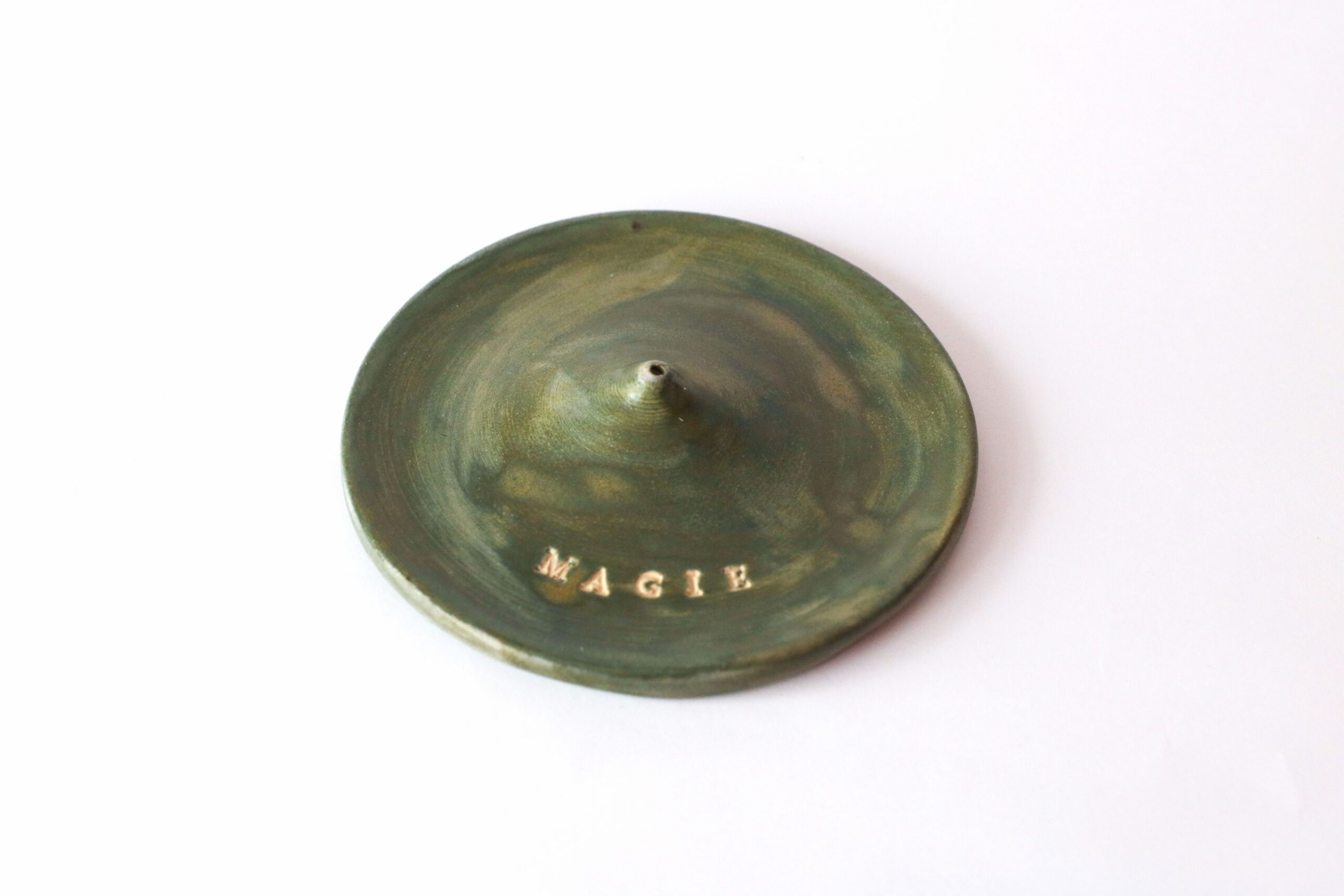 Green ceramic plate with 'MAGIE' text on white background, emphasizing simplicity and elegance.