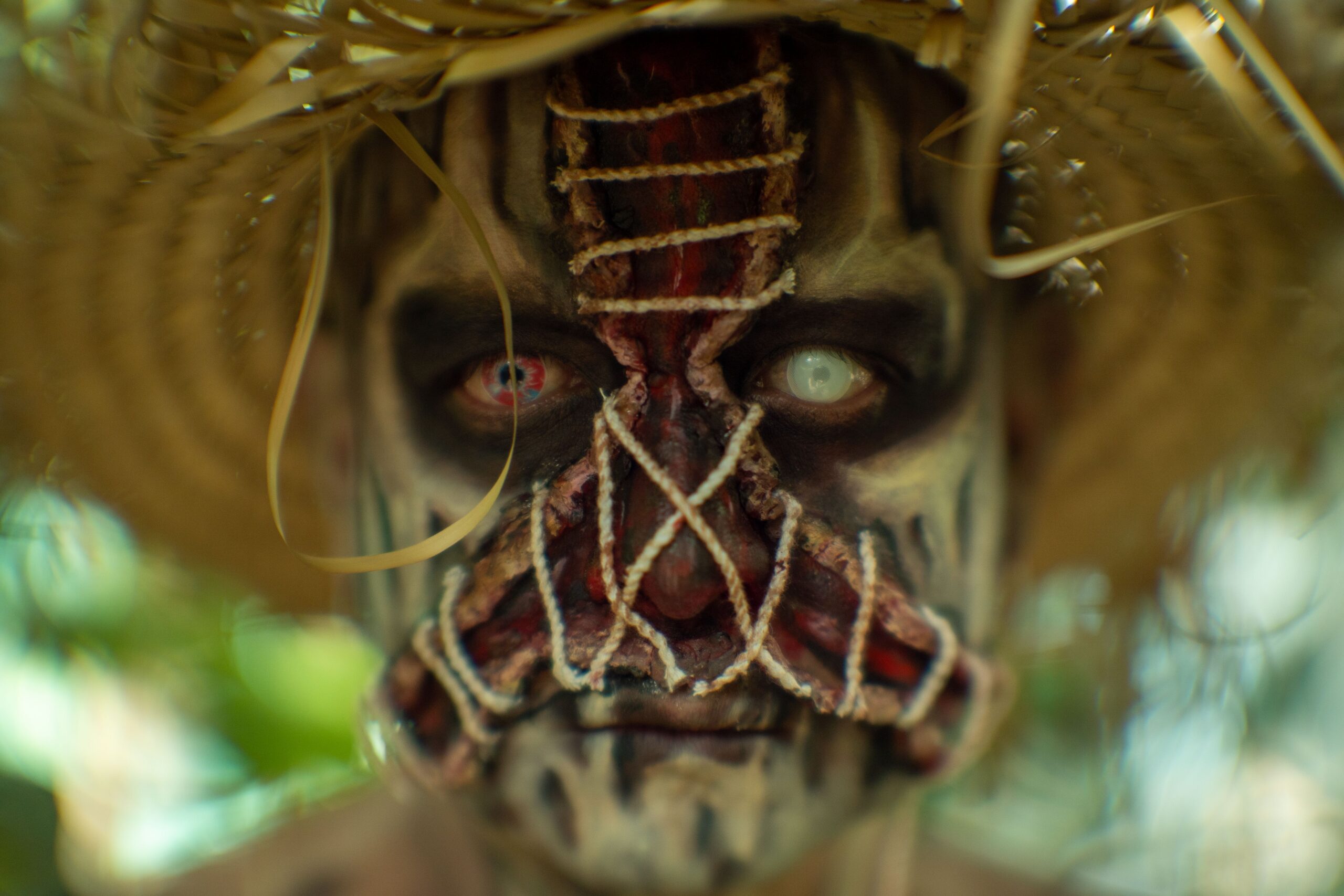 Close-up of a person in eerie Halloween costume and makeup with straw hat outdoors.