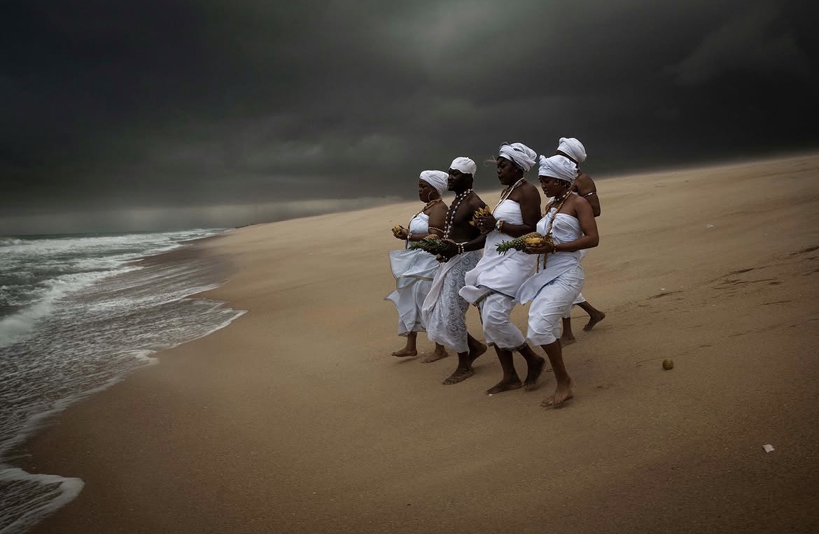 Procession d’initiés vêtus de blanc sur une plage du Bénin, sous un ciel d’orage